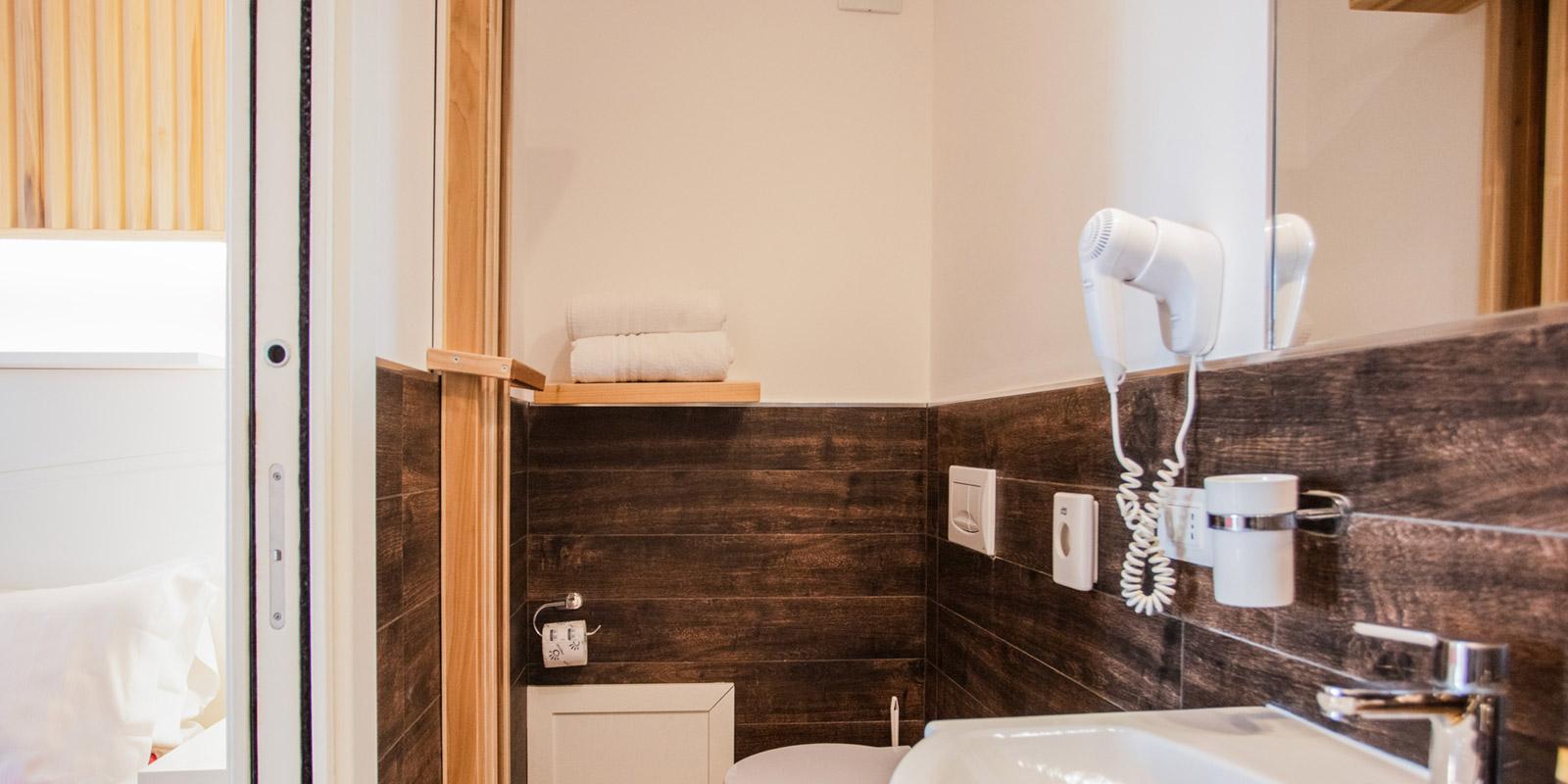 Bagno moderno con sanitari bianchi, asciugacapelli e pareti in legno scuro.