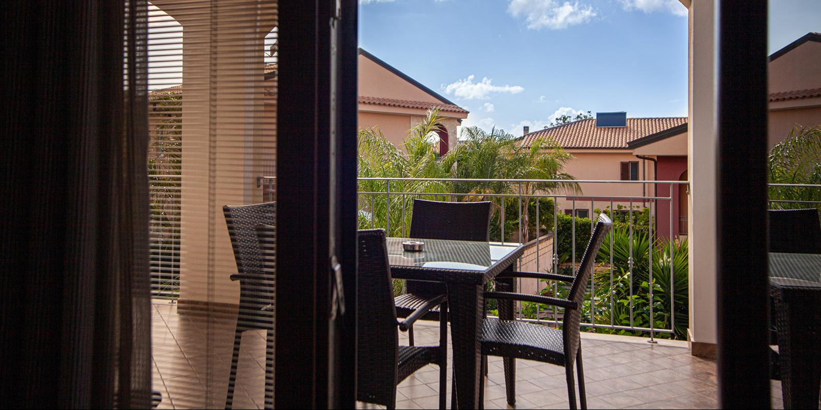 Vista su terrazza con sedie, tavolo e palme, cielo sereno.