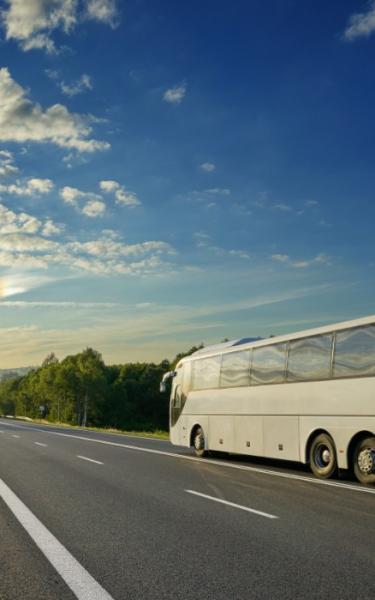 Autobus bianco su strada panoramica al tramonto, cielo azzurro e nuvole.